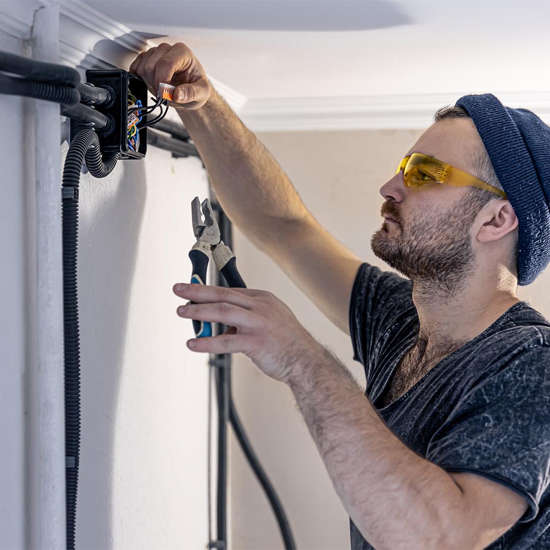 Attractive male electrician repairing an outlet, installing an outlet indoors.